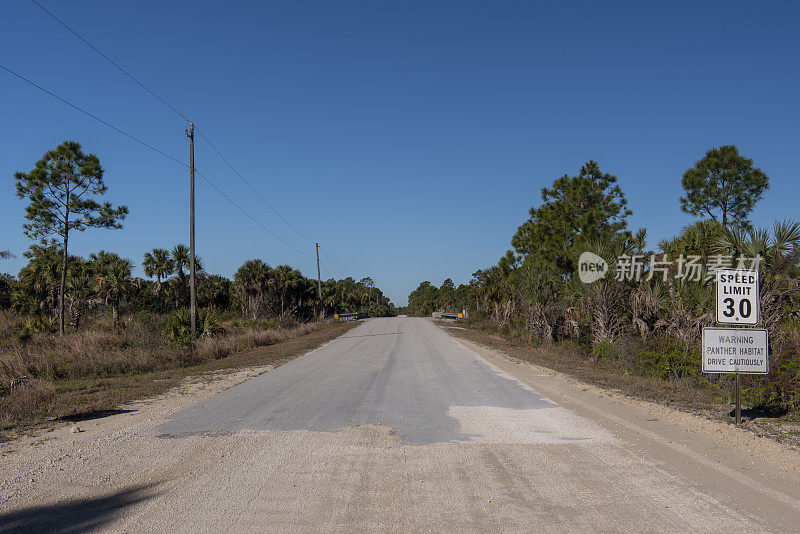 黑豹栖息地警告和30英里每小时的限速标志在退化的空旷道路上，背景是桥梁和森林