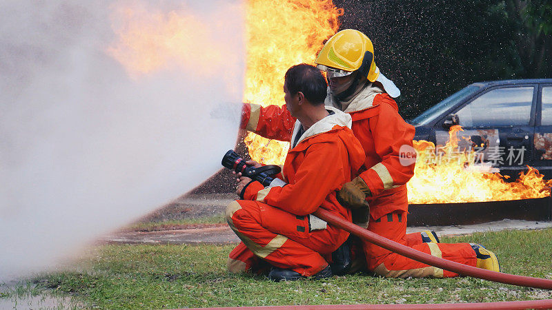 消防救援队员接受灭火器训练。团队合作消防队员使用消防水带化学水泡沫喷雾机与火焰搏斗。消防队员穿安全帽制服