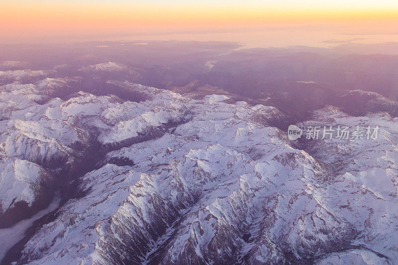 日落时从飞机窗口看到的白雪覆盖的山脉