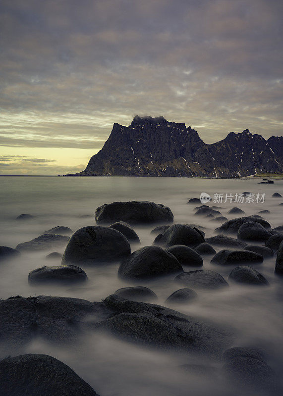 日落时海边的巨大鹅卵石，背景是山脉。