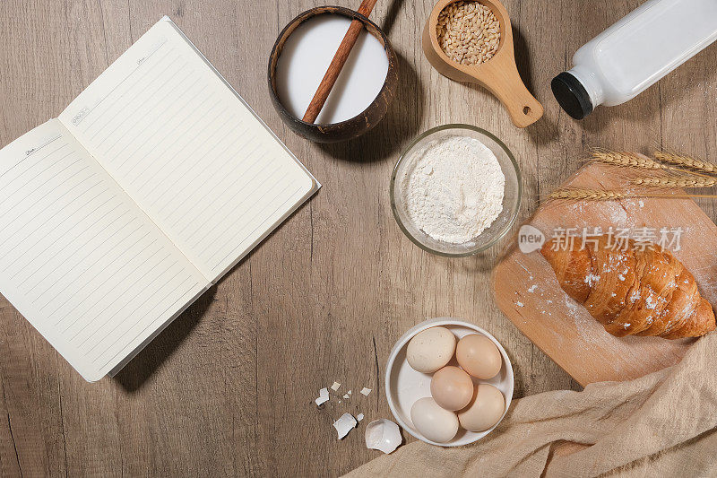一个空白的笔记本旁边打开烘焙蛋糕或糕点的材料平放在木制厨房台面。设计空间，俯视图