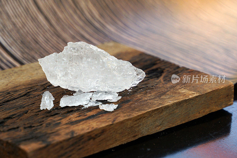 木头背景上的明矾块。它是一种矿物，具有透明的白色晶体，无味，涩味，研磨成类似冰糖的白色粉末。