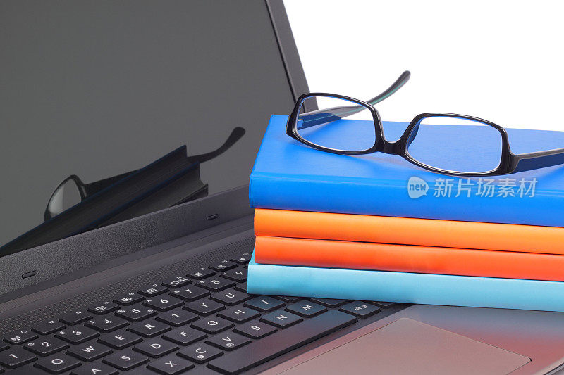 带眼镜的笔记本电脑键盘上的书
