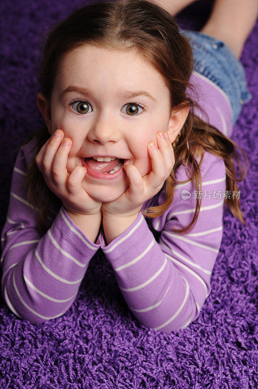 快乐的年轻女孩躺在紫色的地毯上