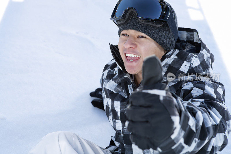 快乐的滑雪者坐在雪地上竖起大拇指