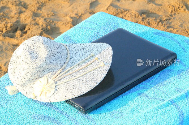 带着太阳帽的笔记本电脑在海滩上