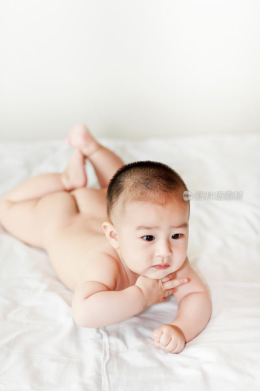 赤裸的可爱的小男孩爬在白色的床上