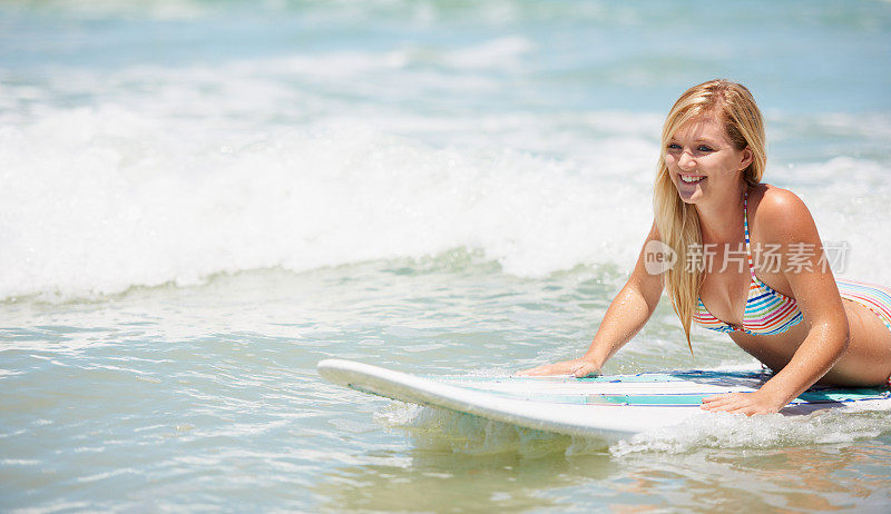 一个年轻漂亮的金发女郎穿着比基尼躺在冲浪板上