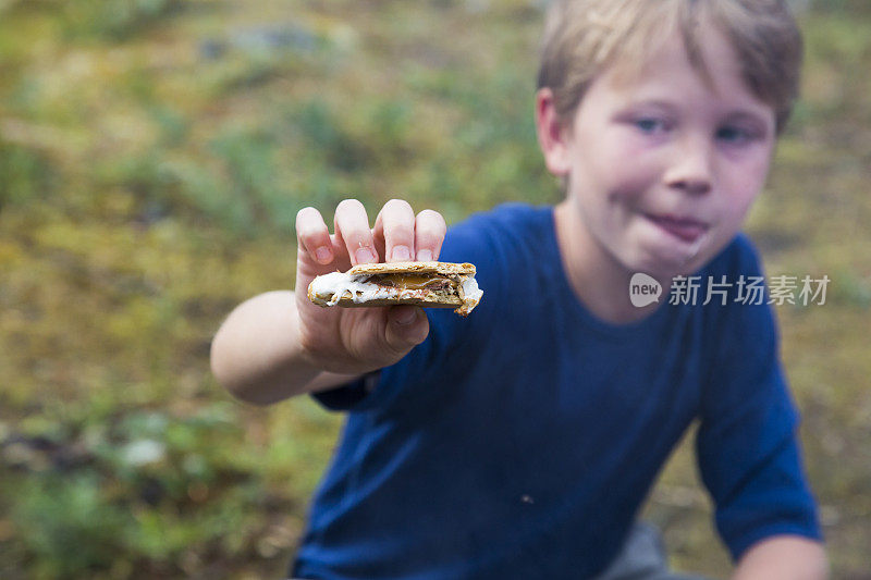 男孩抱着棉花糖，在篝火前舔嘴唇