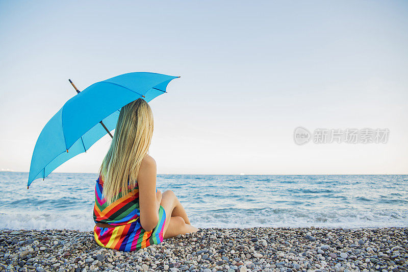 女人拿着阳伞坐在海边看