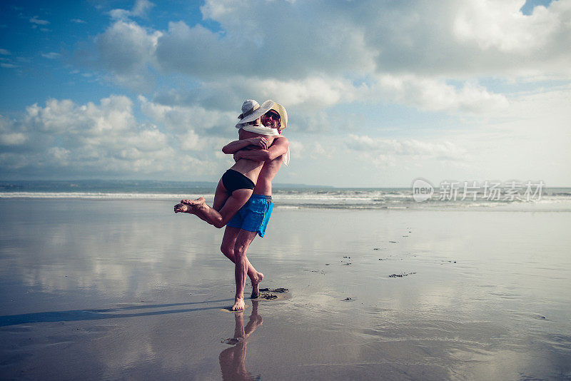 快乐的夫妇有乐趣和在海滩上旋转