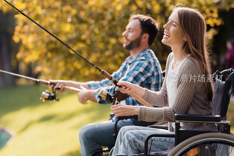 一个女人和一个坐在轮椅上的男人坐在湖边。他们手里拿着纺纱机，正在钓鱼。