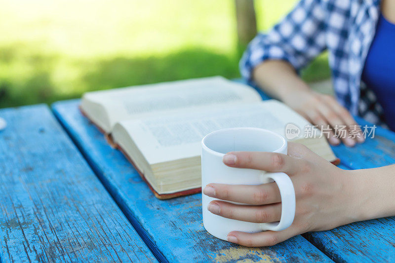 一个女人正在花园里看书和喝咖啡