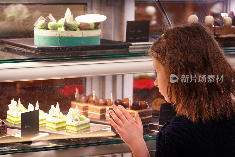 小女孩在糖果店里看橱窗。甜食品种。小企业和儿童的概念