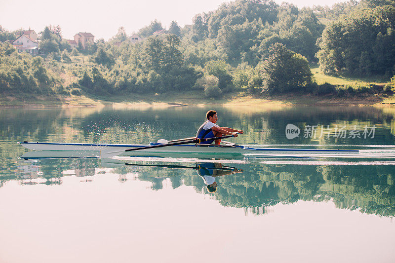 一位年轻的单人赛艇选手在宁静的湖面上划桨