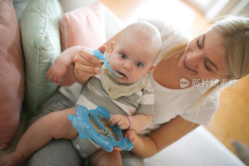 年轻的母亲带着男婴在家给婴儿喂食。关闭了。