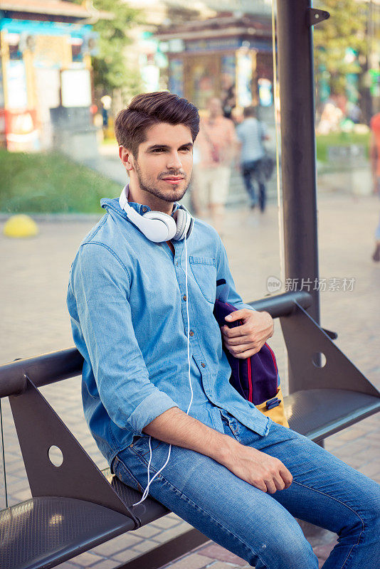 英俊的年轻人坐在公交站等待