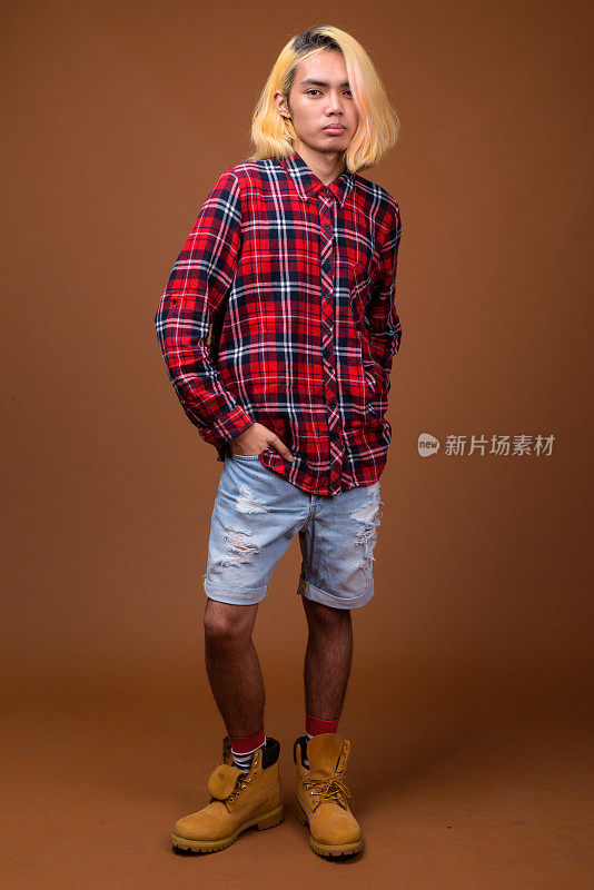 工作室拍摄的年轻亚洲男子穿着时髦的衣服，背景是彩色的
