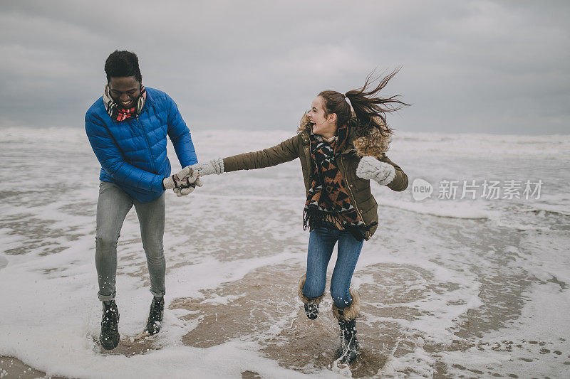 一对年轻夫妇在冬天的海滩上大笑