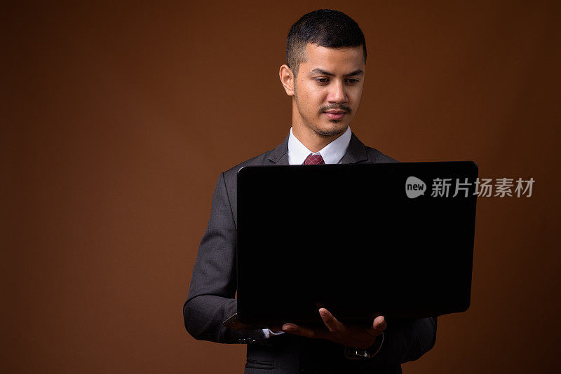 在彩色背景下使用笔记本电脑的年轻亚裔商人的工作室拍摄