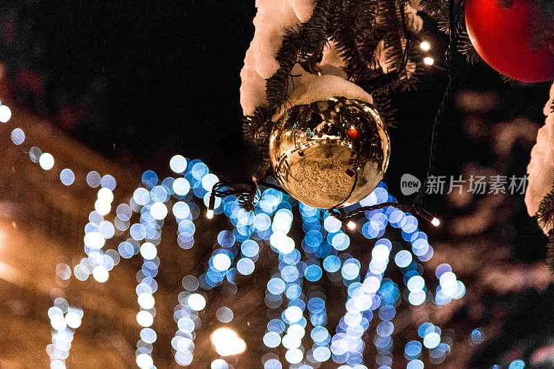 巨大的装饰照明圣诞树在户外的雪在晚上与小装饰品反射