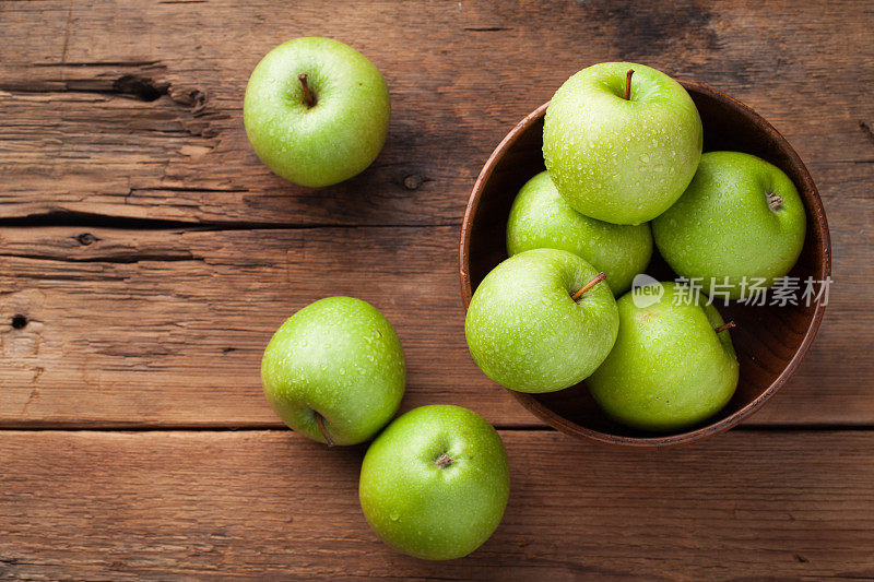 一个木碗里装着成熟的青苹果，放在一张旧的质朴的桌子上。木制背景上有用的水果。顶部视图与复制空间
