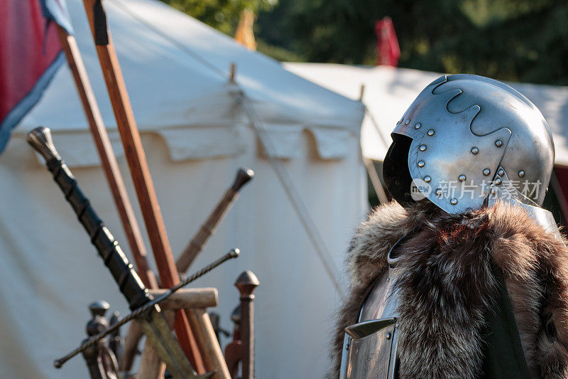 中世纪铁头盔，金属盔甲和毛皮大衣，剑和白色帐篷的背景