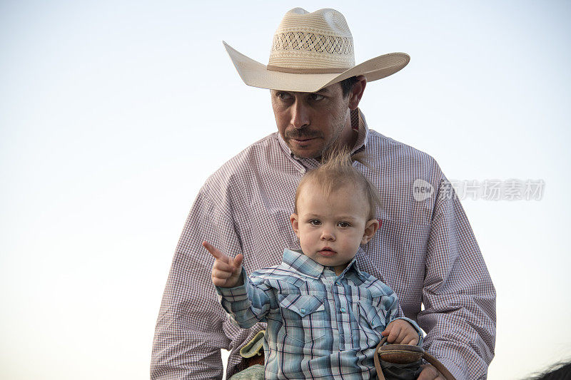 蹒跚学步的孩子与牛仔父亲坐在马和点