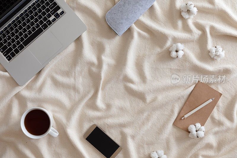 顶视图舒适的冬天背景与笔记本电脑，一杯茶与棉花花，温暖的针织毯子，女性复古的工作空间。生活方式的概念