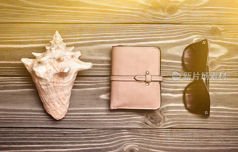 旅行的概念。贝壳，钱包，木制表面上的太阳镜。前视图。平的。