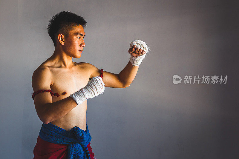 年轻的亚洲拳击手或泰拳战士在灰色背景下出拳和训练，泰拳和武术概念
