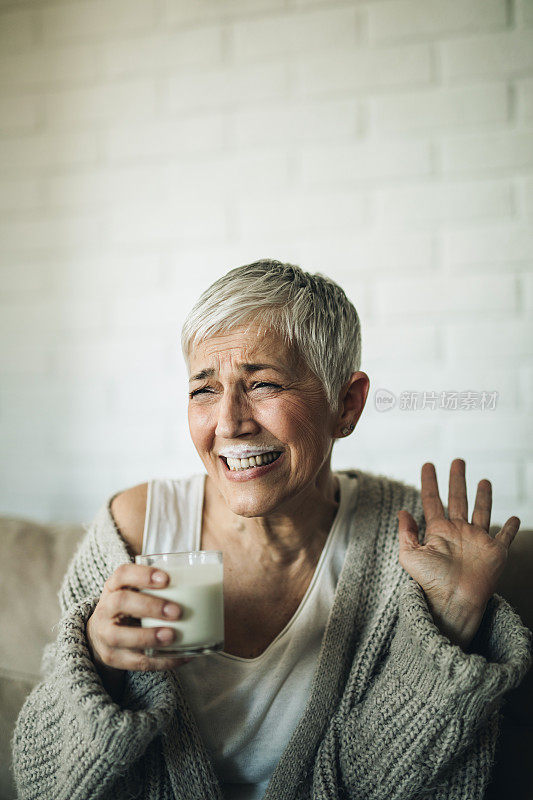 开朗成熟的女人在家里喝牛奶的时候玩得很开心。