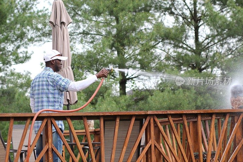 一个非裔美国人站在外面，用水管往甲板上喷水