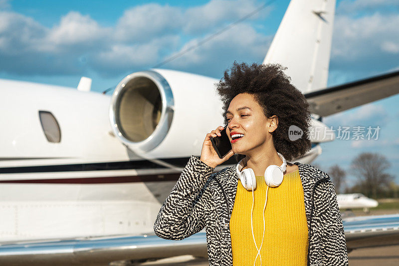 富有的年轻女商人一边打电话一边下停在机场滑行道上的私人飞机