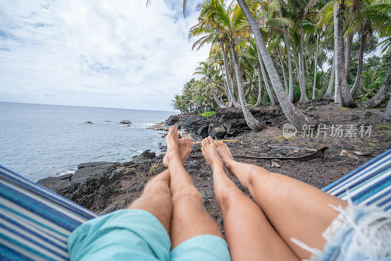 从海滩吊床上的一对夫妇的视角，赤脚。人们旅游热带气候概念。