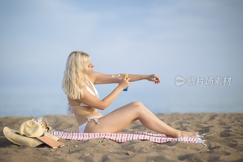 金发女人在海滩上涂防晒霜
