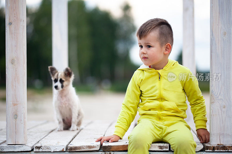 可爱的小男孩和他的狗坐在人行桥上。保护动物。