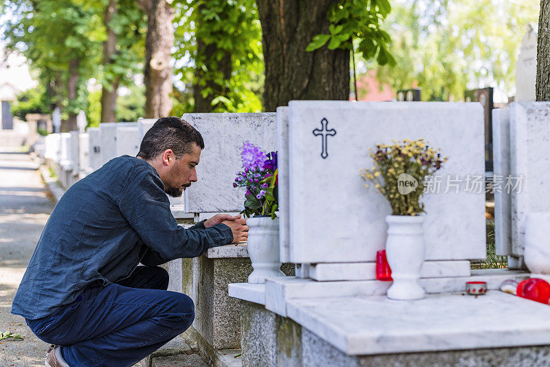 一个黑衣男子跪在他已故朋友的墓前