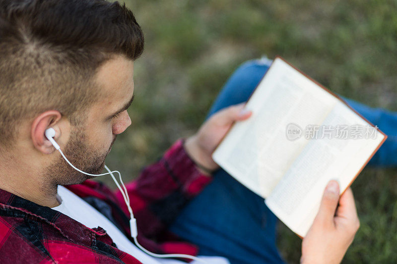 戴着入耳耳机的男人在户外看书