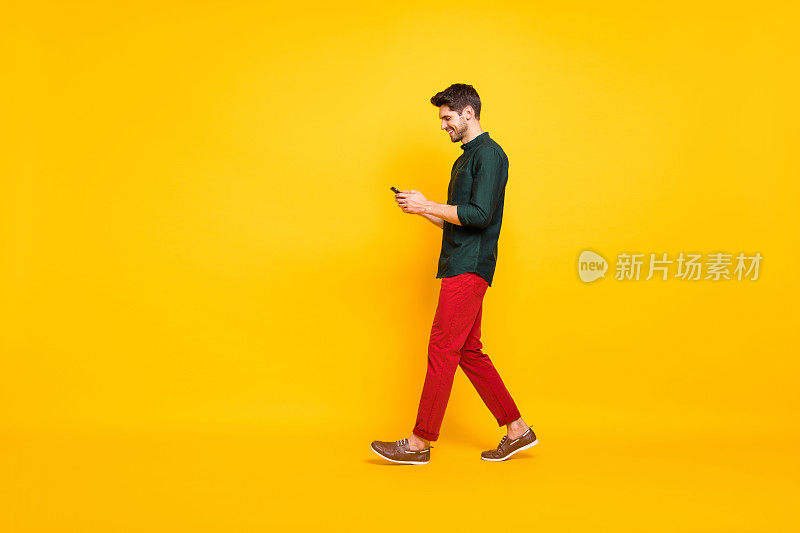 全身尺寸的照片移动愉快的散步上瘾的有吸引力的男人浏览他的电话穿红裤子裤子鞋孤立在黄色鲜艳的颜色背景