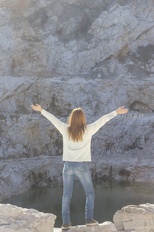 橙色头发的女游客高举双臂，伸开双臂站在废弃的大理石采石场