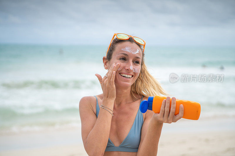 夏日——年轻女子在海滩上涂抹防晒霜，保护皮肤