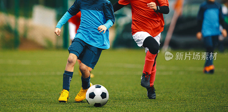 青年足球锦标赛。青年运动员在草地体育场踢足球比赛。两名身穿红衫和蓝衫的少年足球运动员争夺足球