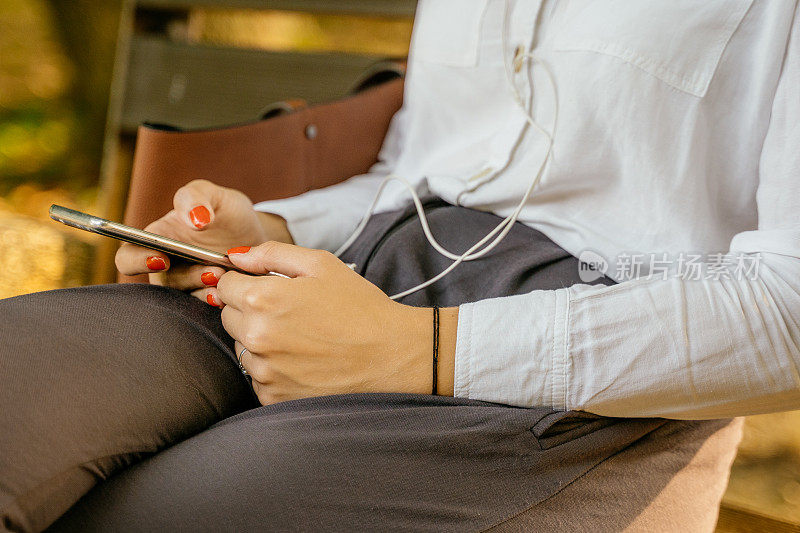 女人坐在长椅上玩智能手机的画面