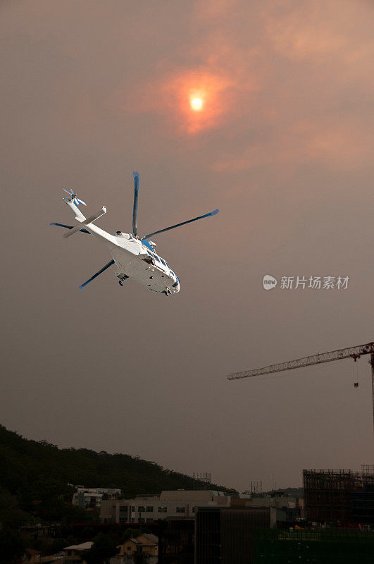 森林大火的日落天空，一架空中直升机在前景。太阳透过野火的烟雾和薄雾照耀着高斯福德市。2019年澳大利亚。