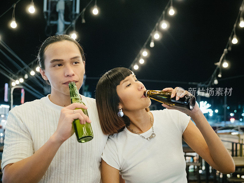 年轻的亚洲夫妇在屋顶派对上喝啤酒