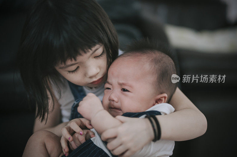 一个亚裔中国小妹妹照顾着，说话，抱着她正在哭的小弟弟