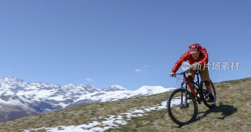 骑山地车的人在白雪覆盖的山峰上骑下田野