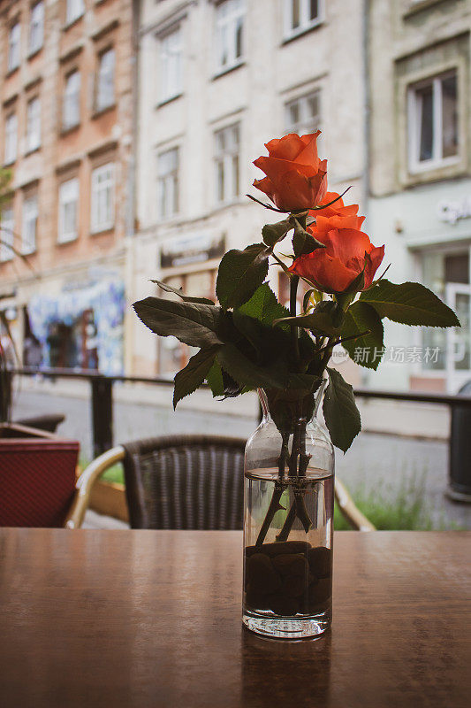 户外餐厅桌上花瓶中的红玫瑰，烘托形象。花桌装饰用鲜花，过滤。美丽的玫瑰映衬着空旷的街道。