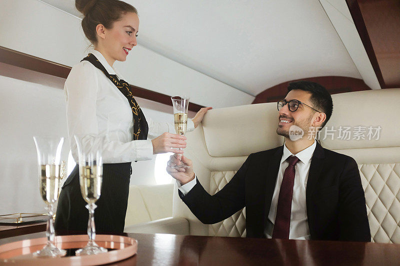 年轻的亿万富翁坐头等舱，空姐给他端来一杯香槟庆祝他的商业成功